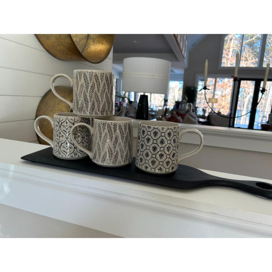 Set of four patterned mugs on a black tray against a home interior background
