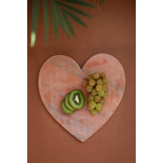 Heart-shaped marble cutting board with sliced kiwi and grapes on a brown background